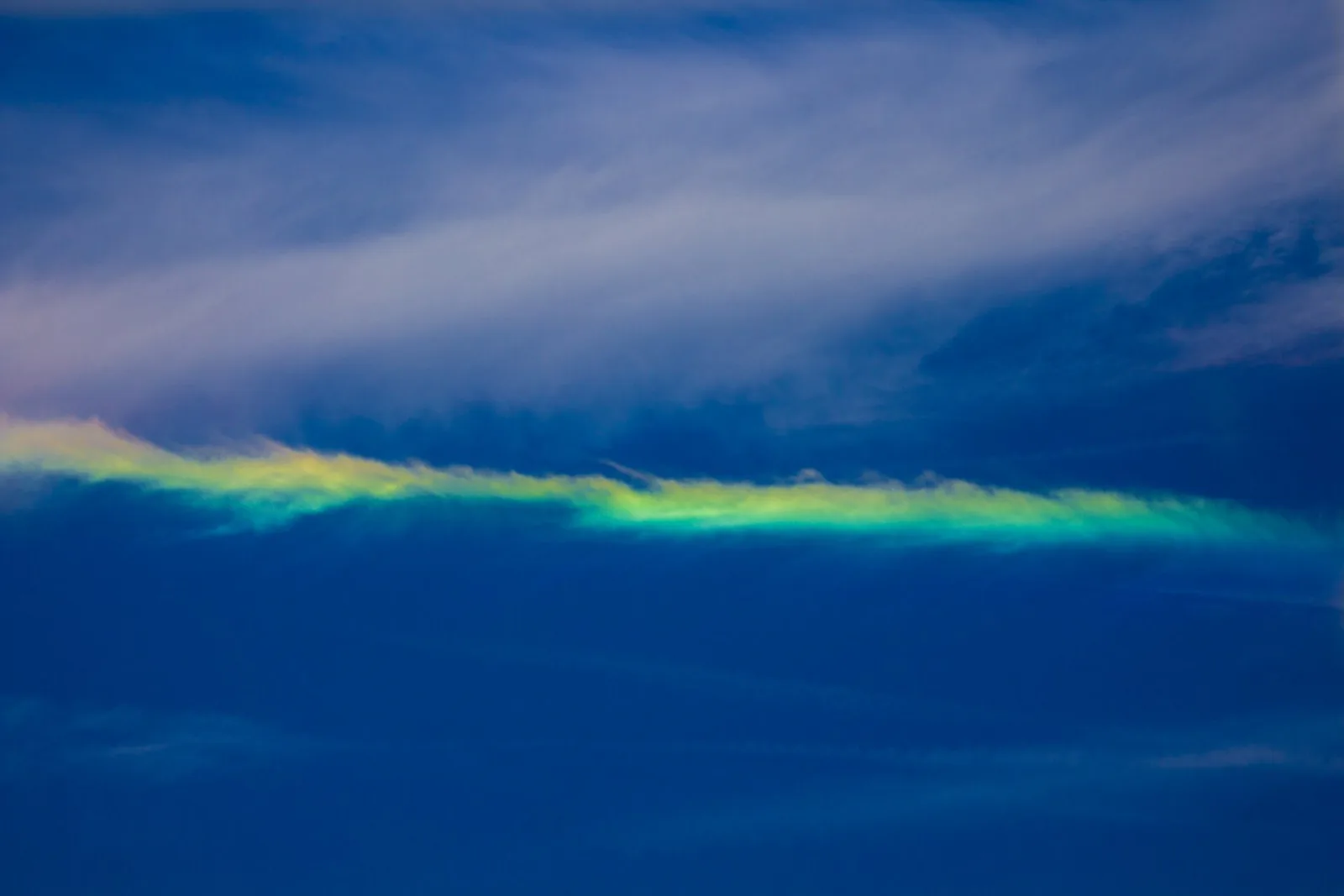 A flat band of rainbow colors running through thin clouds in a blue sky